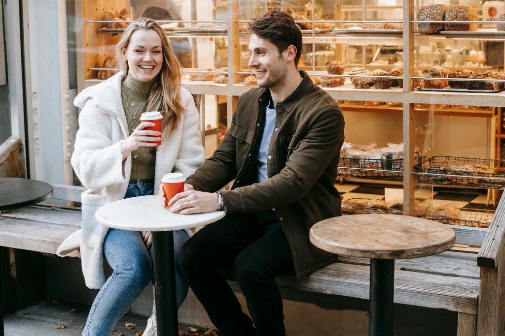 Young couple enjoying coffee at a modern outdoor cafe on a bright day.